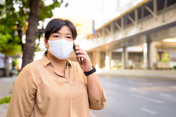 Overweight Asian woman with mask for protection from corona virus outbreak talking on the phone