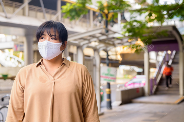 Overweight Asian woman thinking with mask for protection from corona virus outbreak in the city