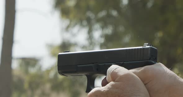 Slow motion of a man firing a hand gun in a firing range with cartridge flying away