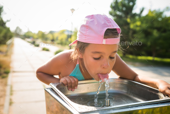 Cute thirsty girl drinks water from drinking sink - Stock Photo - Images