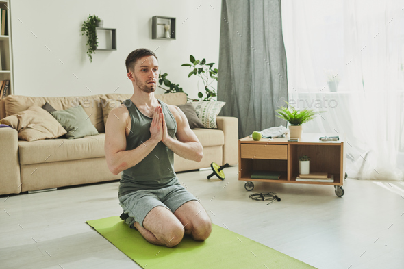 Calm guy in activewear standing on his knees with hands put together by chest - Stock Photo - Images