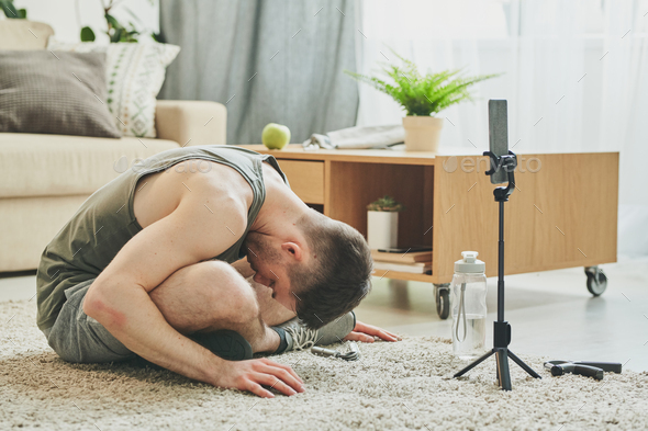 Young active man with crossed legs bending forwards while sitting on the floor - Stock Photo - Images