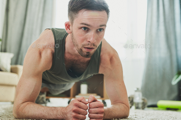 Young man in sportswear standing in plank while exercising on the floor - Stock Photo - Images