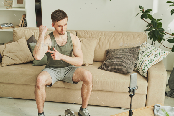 Young athlete on couch boasting with his power while pointing at his bicep