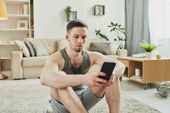 Young serious sportsman in activewear sitting on the carpet in living-room - Stock Photo - Images