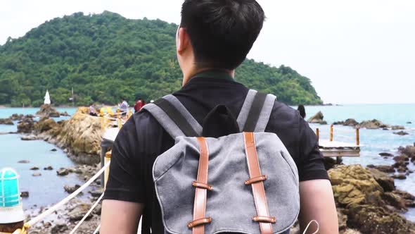 Follow Shot of Rear View Portrait of a Young Asian Man Walking at Beach with Bag alt