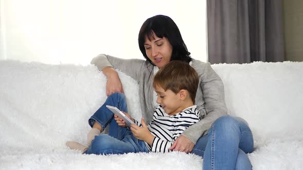 A Mother or Nanny Spends Time with a Pre-school Child Using a Tablet. The Concept of a Happy Family alt