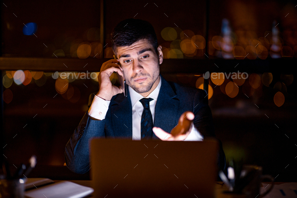 Displeased Entrepreneur Talking On Cellphone Sitting In Office At Night - Stock Photo - Images