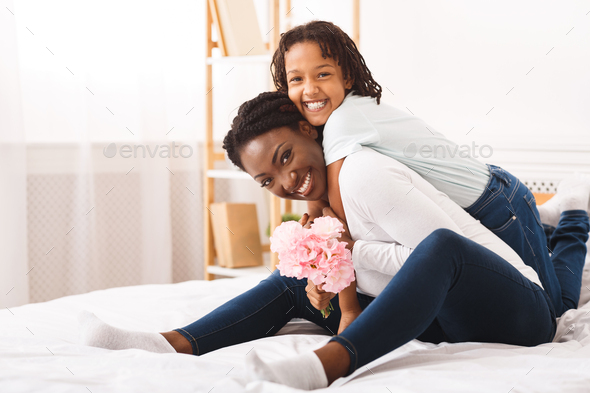 Black girl congratulating her mom with flowers at home