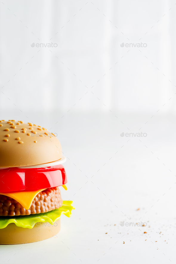 Artificial plastic burger with meat cutlet, tomatoes slice and green salad on a light grey - Stock Photo - Images