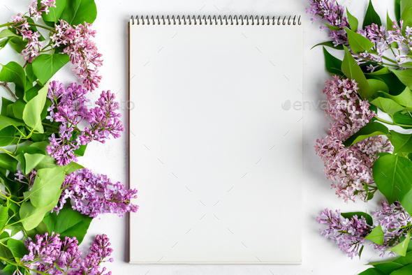 Holiday festive card from fresh lilac flowers and paper notebook on a light grey marble background - Stock Photo - Images