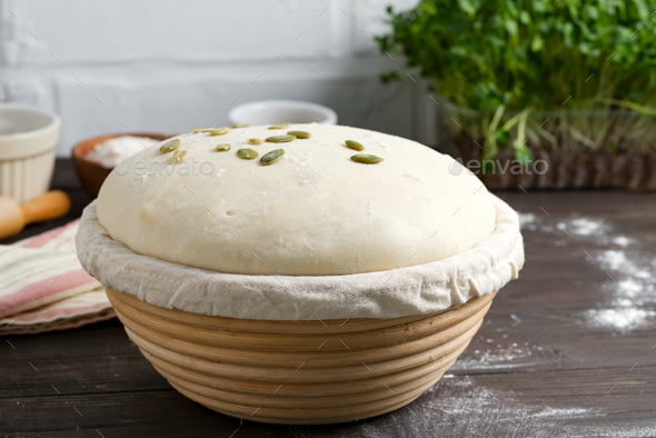 Homemade freshly prepared yeast dough in a basket for baking with pampkin seeds on a dark wooden - Stock Photo - Images