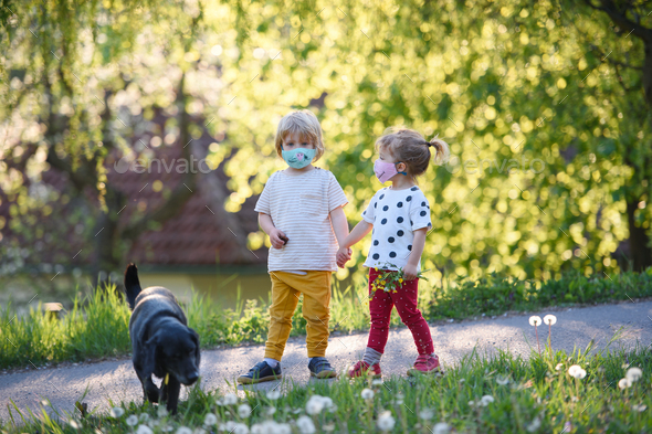 Small children with face masks and dog playing outdoors, coronavirus concept