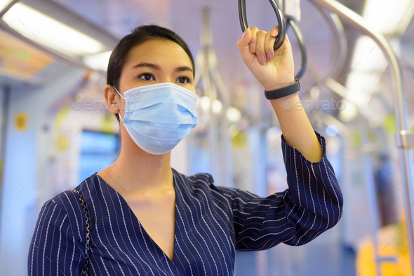 Young Asian businesswoman with mask for protection from corona virus outbreak riding the train - Stock Photo - Images