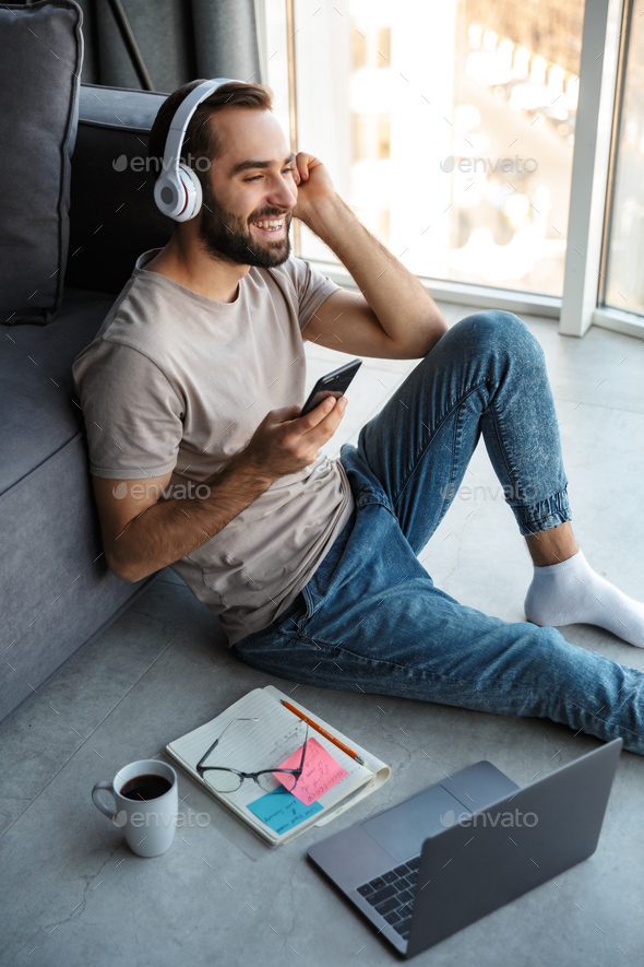 Attractive smart young man sitting on a floor in the living room - Stock Photo - Images