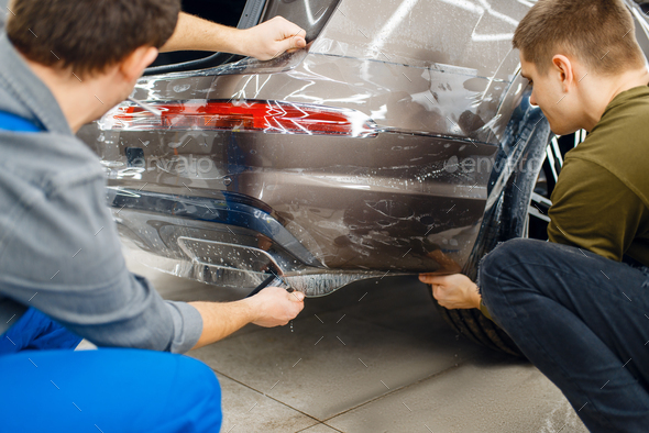 Two workers applies car protection film on bumper - Stock Photo - Images