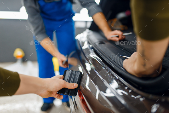 Two workers smoothes car protection film on bumper - Stock Photo - Images