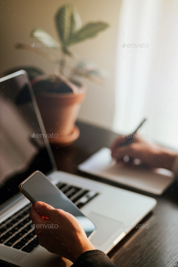 office worker browsing phone and laptop indoors - Stock Photo - Images