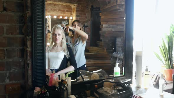 Professional  Hairdresser at work in salon, woman-stylist makes a hairstyle for a cute blond girl