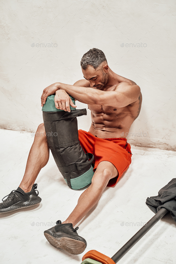 Handsome adult sportsman wearing sportswear posing for a camera while holding a weight bag - Stock Photo - Images