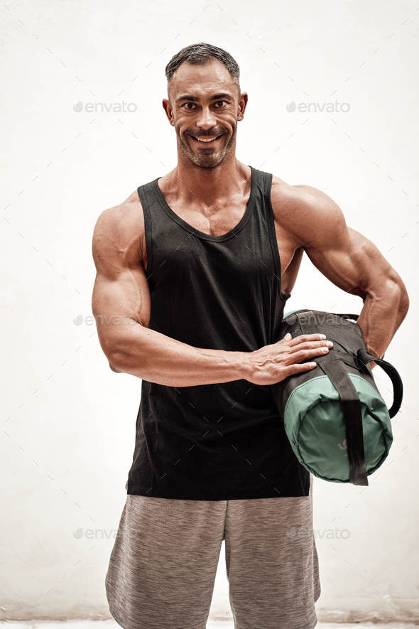 Strong and muscular athlete posing in a bright studio with a weight bag looking fresh - Stock Photo - Images