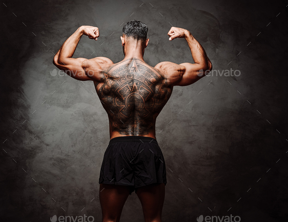 Close-up photo of a shirtless inked sportsman, standing backwards, in a dark studio - Stock Photo - Images