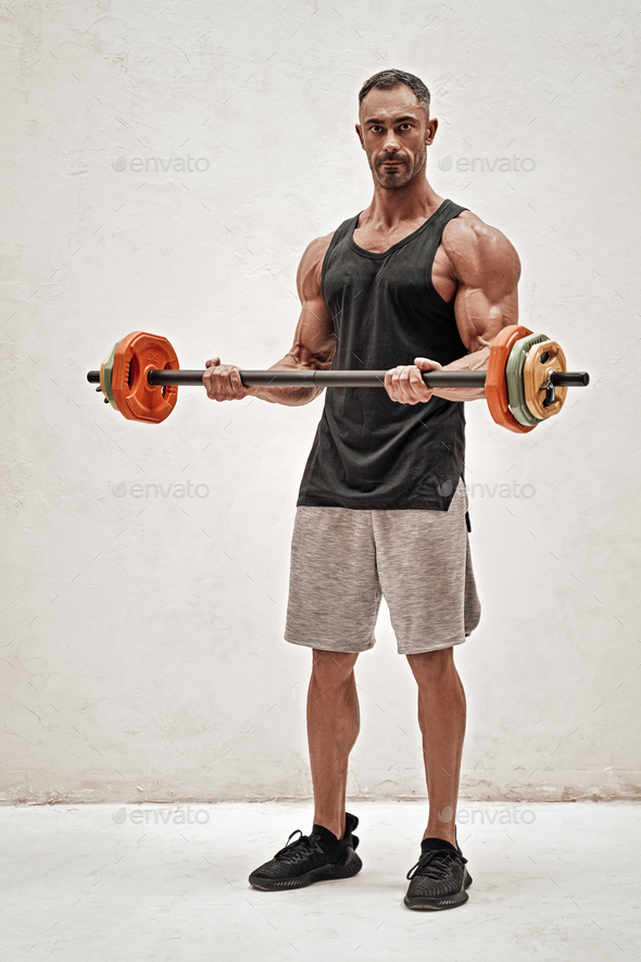 Full height portrait of a sportsman, flexing with a barbell in a bright studio - Stock Photo - Images