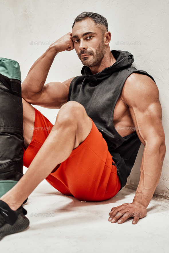 Close-up photo of a sportsman, leaning on the wall near fitness gear looking exhausted - Stock Photo - Images