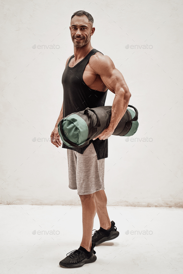 Buffed sportsman posing in a bright studio with a weight bag - Stock Photo - Images
