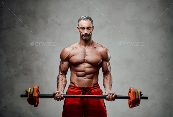 Shirtless adult male bodybuilder doing a biceps exercise with a barbell in a bright studio - Stock Photo - Images