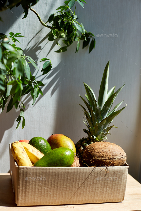 Assortment of organic exotic fruits in box, sunlight.