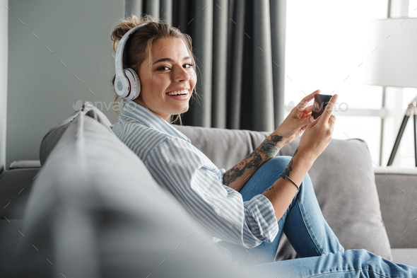 Image of smiling woman using cellphone and headphones while sitting