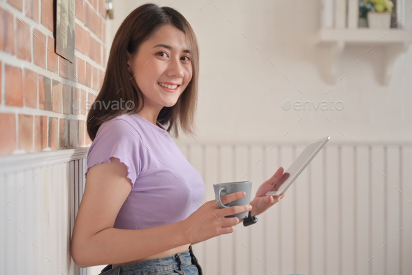 Young female with coffee sitting comfortably was using tablet for video calling with friends. - Stock Photo - Images