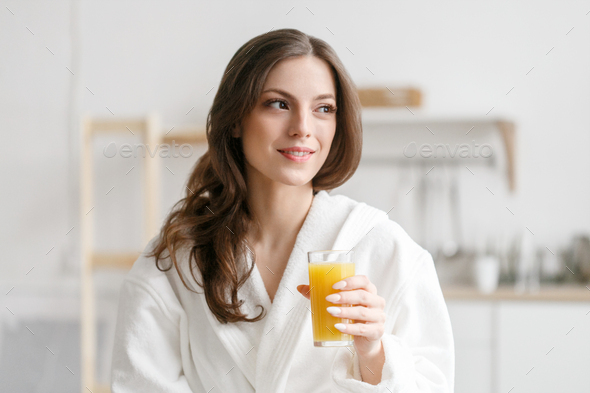 Woman in morning with fresh orange juice in hand. A female in white bathrobe drinking orange juice - Stock Photo - Images