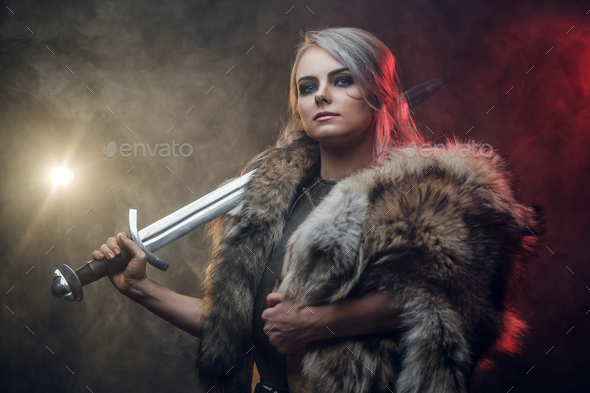 Portrait of a beautiful warrior woman holding a sword wearing steel cuirass and fur - Stock Photo - Images