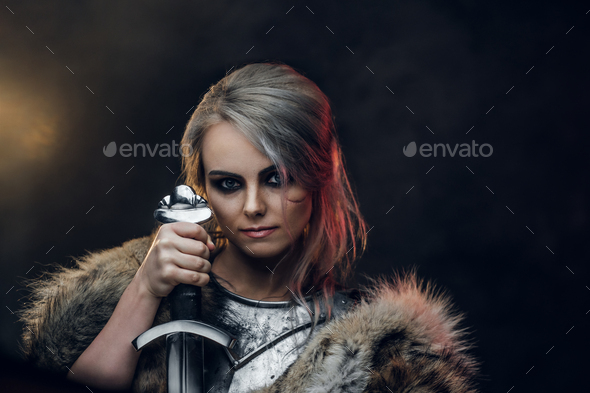 Portrait of a beautiful warrior woman holding a sword wearing steel cuirass and fur - Stock Photo - Images