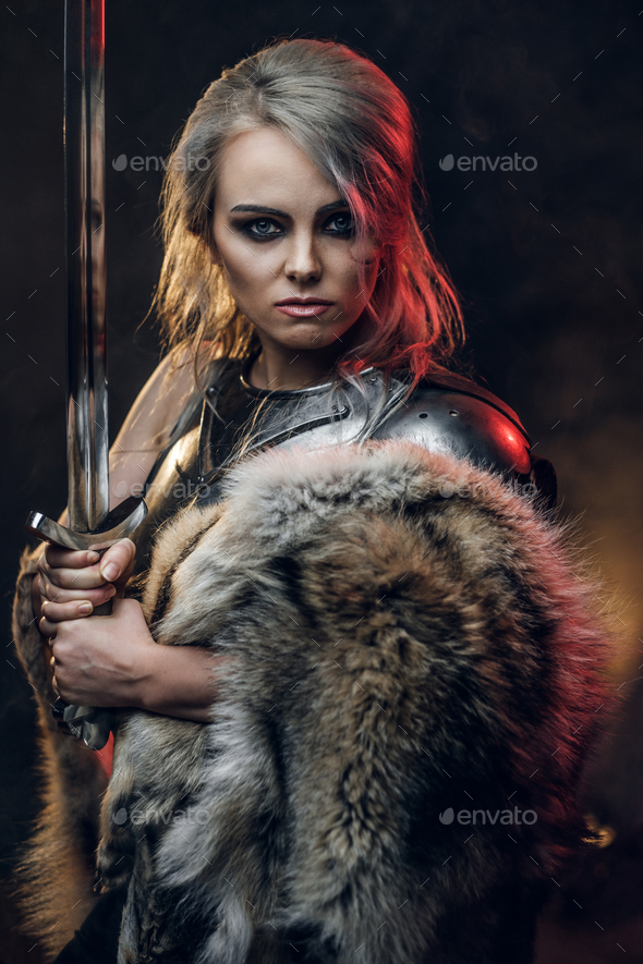 Portrait of a beautiful warrior woman holding a sword wearing steel cuirass and fur - Stock Photo - Images