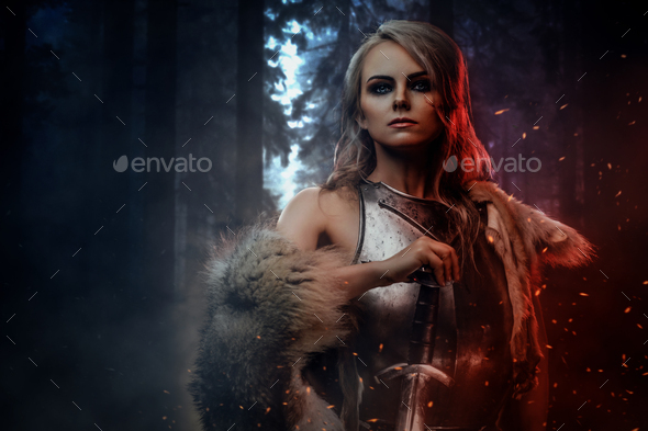 Beautiful warrior woman holding a sword wearing steel cuirass and fur in night forest - Stock Photo - Images