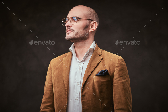 Successfull well-dressed mature bald businessman posing for camera in a dark studio - Stock Photo - Images