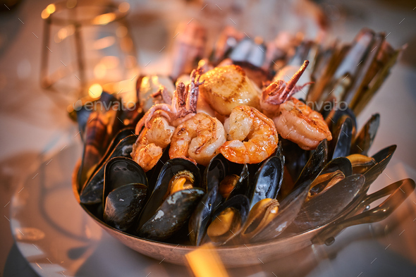 A bowl of grilled shrimps and mussels served on a stone table next to golden candle in a restaurant - Stock Photo - Images