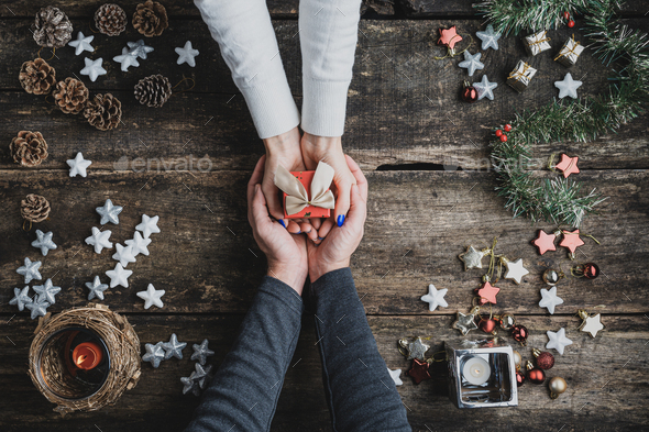 Top view of a male hands cupping female hands holding small red holiday gift box - Stock Photo - Images