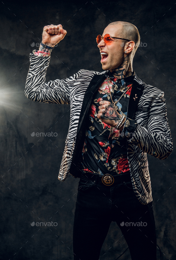 Daring tattooed, bald fashionable male model posing in a studio for the photoshoot showing biceps - Stock Photo - Images