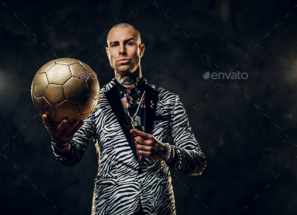 Elegant tattooed male model posing with a golden soccer ball in a studio - Stock Photo - Images