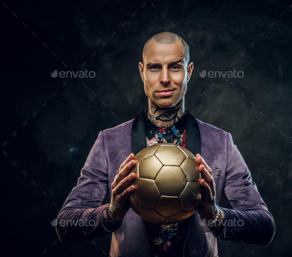 Elegant tattooed male model posing with a golden soccer ball in a studio - Stock Photo - Images
