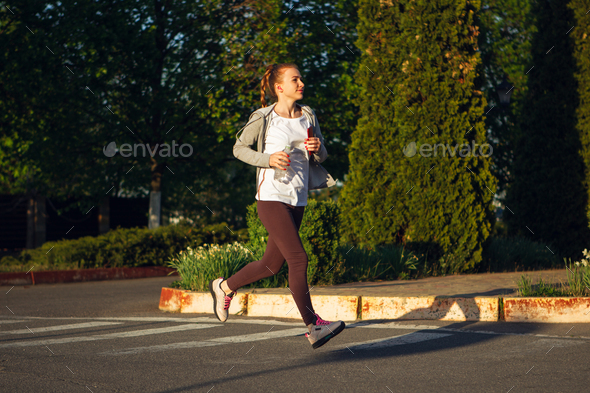 Young female runner, athlete is jogging in the city street in sunshine. Beautiful caucasian woman - Stock Photo - Images