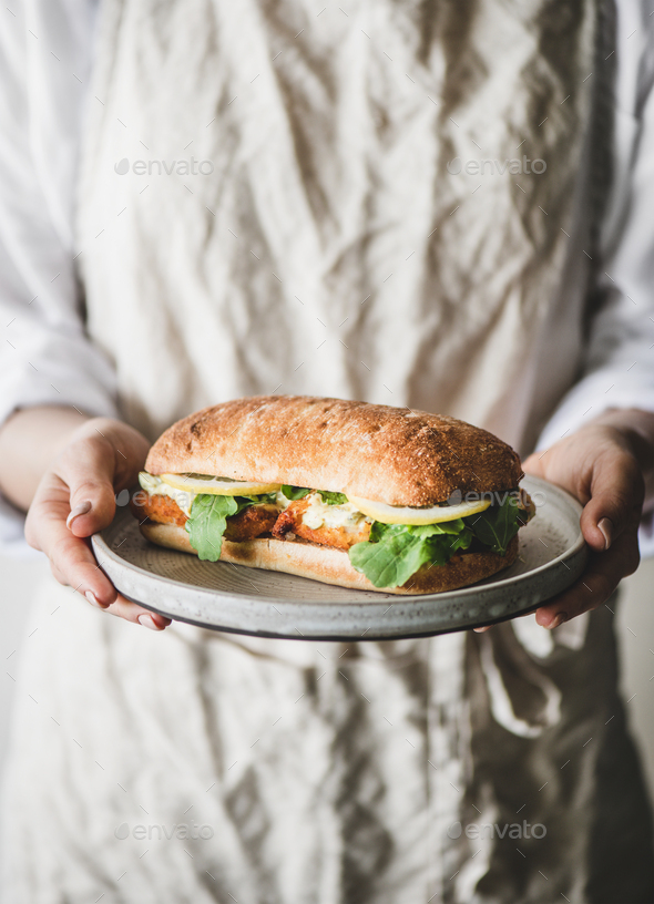 Woman in linen apron holding breakfast sandwich with fried fish - Stock Photo - Images