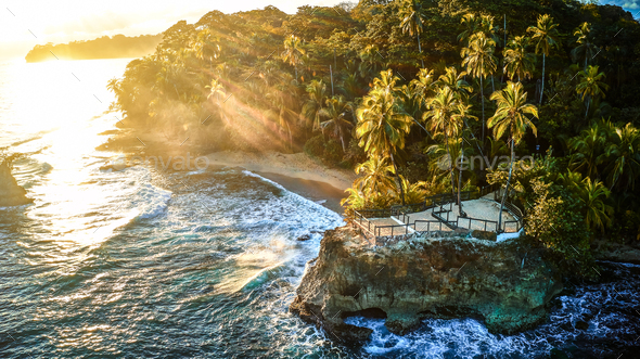 Scenic aerial shot of a tiny rock island surrounded by waves of the crystal clear ocean - Stock Photo - Images