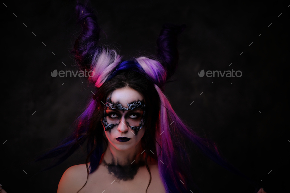 Young woman wearing fantasy dark make-up and violet horns posing in a studio - Stock Photo - Images
