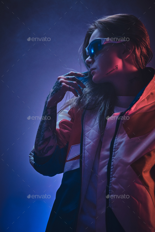 Inked attractive female posing in a neon vivid lights of a studio surrounded by smoke - Stock Photo - Images