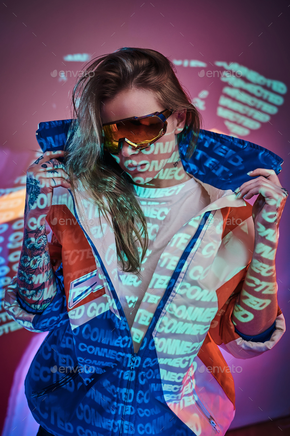 Close up portrait of a young tattooed racer woman posing in a vivid neon studio over text projection - Stock Photo - Images